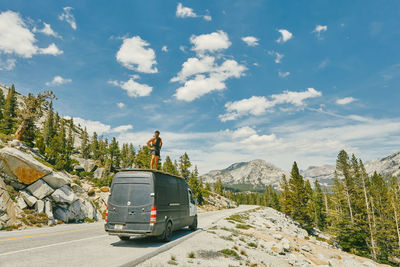 Young man standing on camper van watching views of yosemite park.