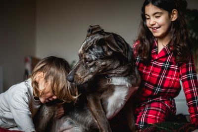 Two children in pajamas play with grey dog sitting on the bed