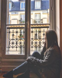 Side view of woman sitting on window sill