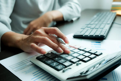 Midsection of businesswoman using calculator at table