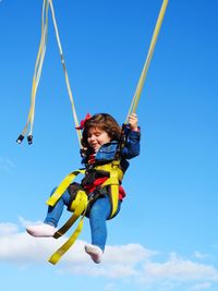 Low angle view of girl bungee jumping against blue sky