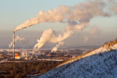 Smoke emitting from factory against sky during winter