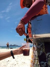 Man holding umbrella on beach against sky