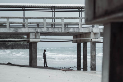Side view of man standing under bridge at beach