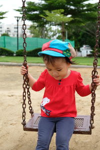 Cute girl looking down while sitting on swing in playground