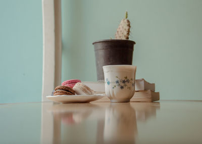 Surface level of macaroons in plate by coffee cup on table