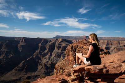 Woman sitting on rock against blue sky