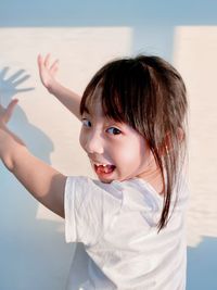 Portrait of girl with arms raised against wall