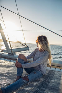 Woman sitting on boat sailing in sea against sky during sunset