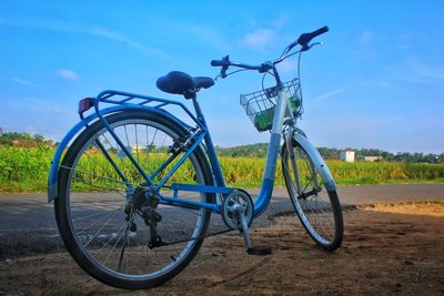 Bicycle parked on field by road against sky