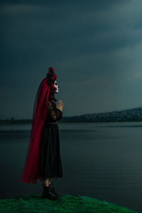 Side view of woman with red umbrella standing against sky