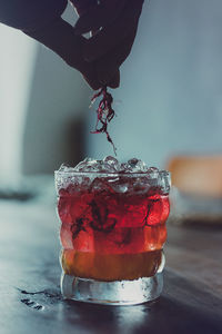 Cropped hand holding flower over drink on table