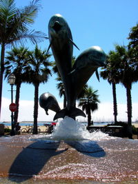 View of statue by palm tree against clear blue sky