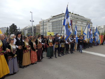 People in traditional clothing with flags standing on road in city