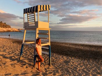 Rear view of woman on beach against sky during sunset