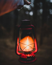 Cropped hand holding lit lantern at night