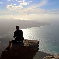 Rear view of man sitting on rock looking at sea