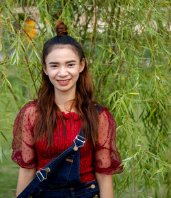 Portrait of smiling young woman standing against plants