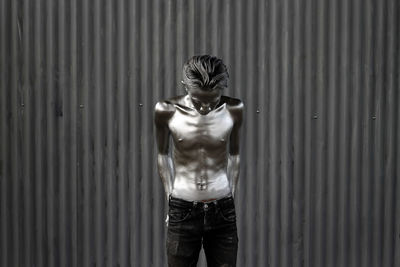 Shirtless man with painted body standing against corrugated iron