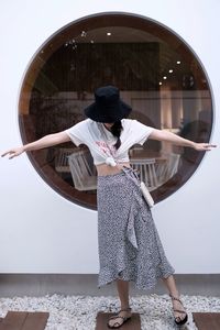 Portrait of woman standing against wall wearing black hat.