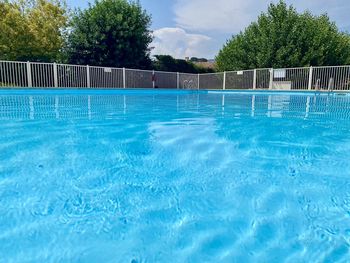 Swimming pool by trees against blue sky