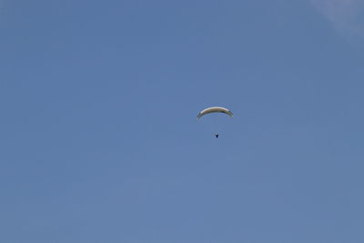 Low angle view of people paragliding against clear blue sky