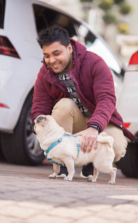 Full length of smiling man stroking dog while crouching outdoors