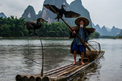 Man with birds on wooden rafts in lake against mountains