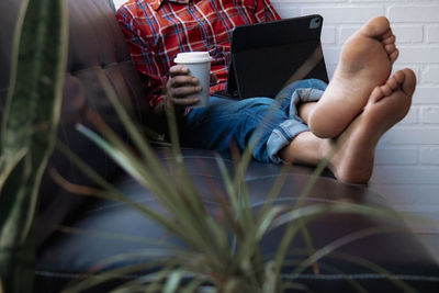 Relaxed man on sofa drinking take away coffee and using digital tablet