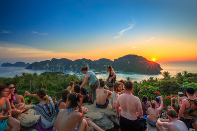 Group of people enjoying at beach against sky during sunset