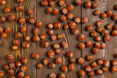 Many hazelnuts with shells evenly spread out on brown wooden surface