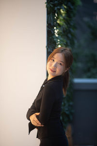 Portrait of young woman standing against wall