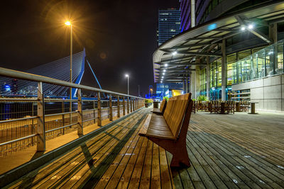 Benches at promenade by erasmusbrug against sky at night