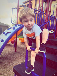 Cute boy sitting on slide at playground