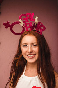 Portrait of smiling teenage girl wearing headdress against pink wall