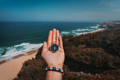 Cropped hand of man holding compass against sea