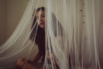 Portrait of young woman sitting on bed in mosquito net at home