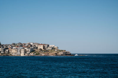 Sea by buildings against clear blue sky