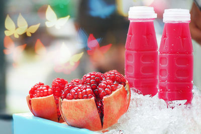 Close-up of pomegranate with juice bottles in tray against window