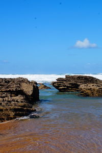 Scenic view of rocks on beach against blue sky