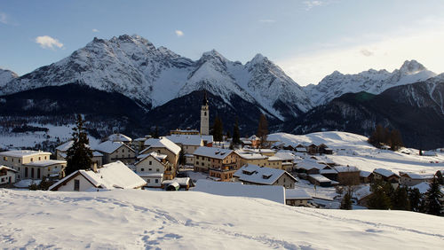 Houses and snowcapped mountains against sky during winter