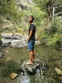 Full length of young woman standing by river in forest