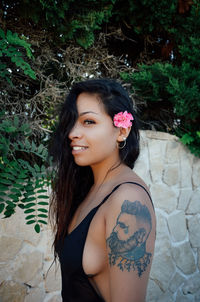 Side view portrait of woman in swimsuit with tattoo on arm standing outdoors