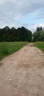 Dirt road passing through agricultural field against sky