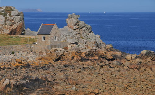 Rocks on sea by buildings against sky