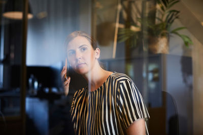Creative businesswoman talking on mobile phone seen through glass in office