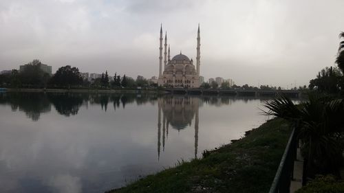 Mosque by reflection lake against sky