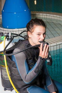 Portrait of young woman in diving suit sitting in swimming pool