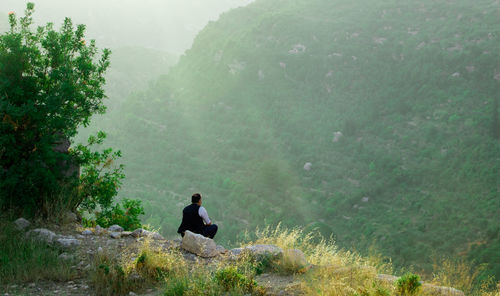 Man sitting on rock against mountain