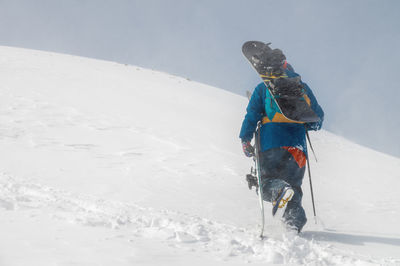 Man with ski equipment and a snowboard climbs a snowy mountain. blue sky and snowy mountain in the